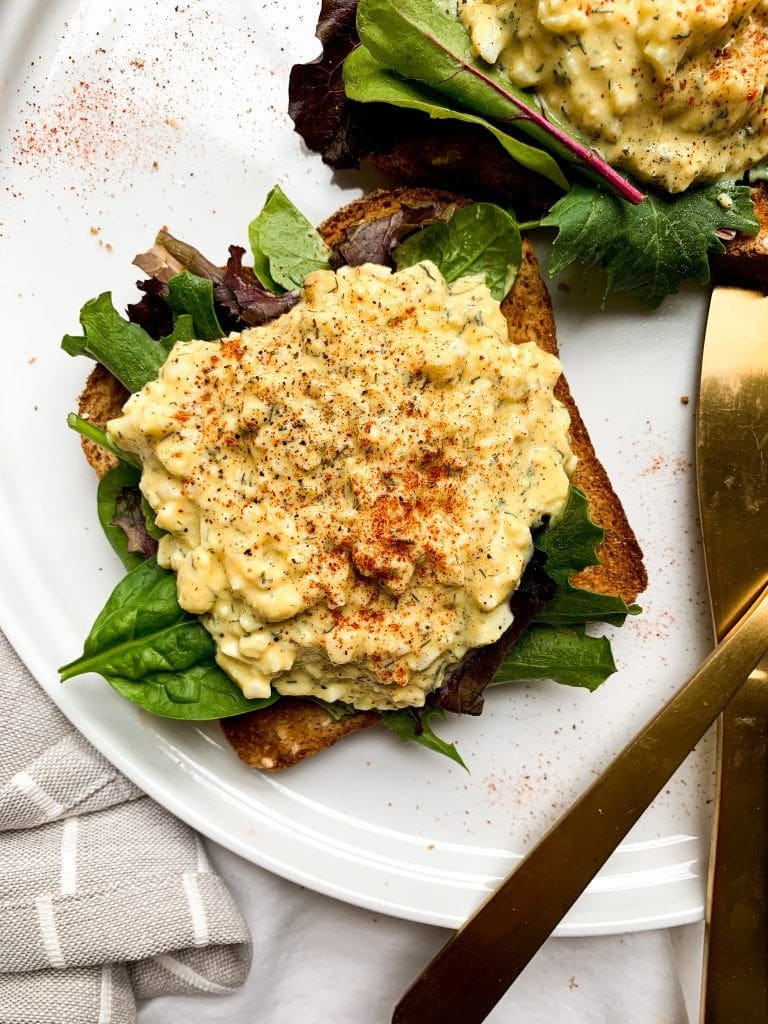 two piecse of toast topped with healthy egg salad and greens