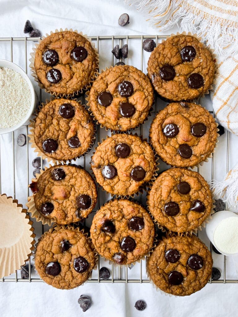 11 pumpkin protein muffins on wire rack next to muffin liners