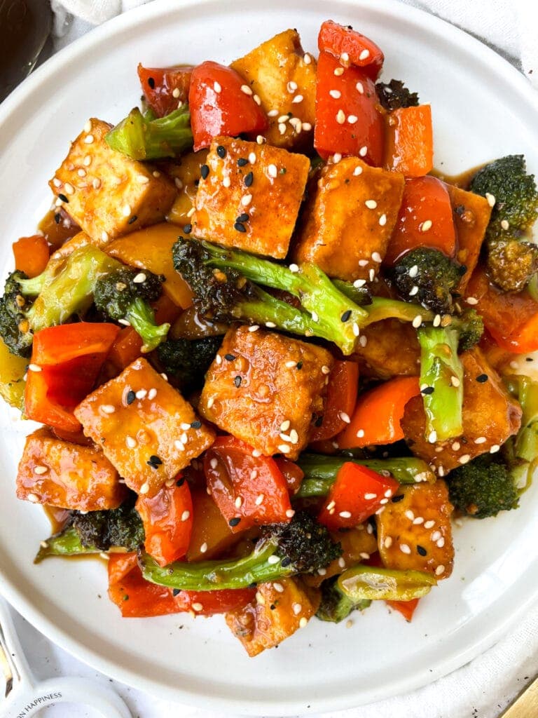 top view of orange tofu topped with sesame seeds on a white plate