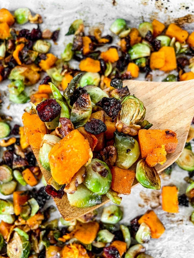 roasted butternut squash and brussels sprouts on a sheet pan and wooden spoon