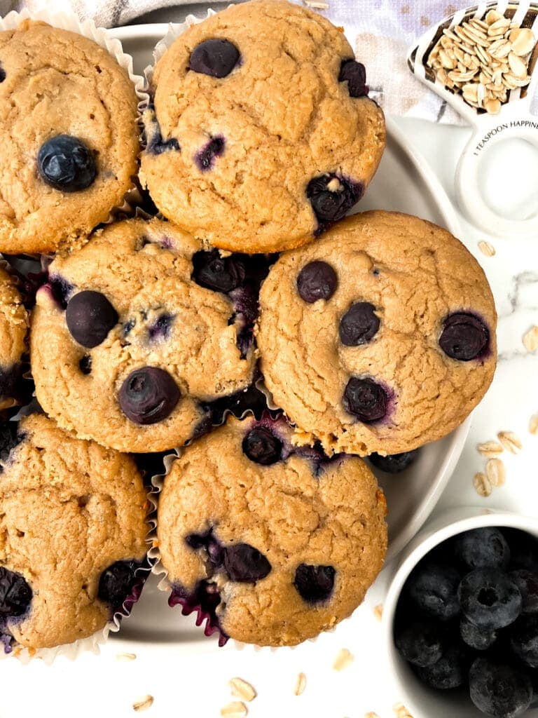 oat flour blueberry muffins on a plate next to oats and berries