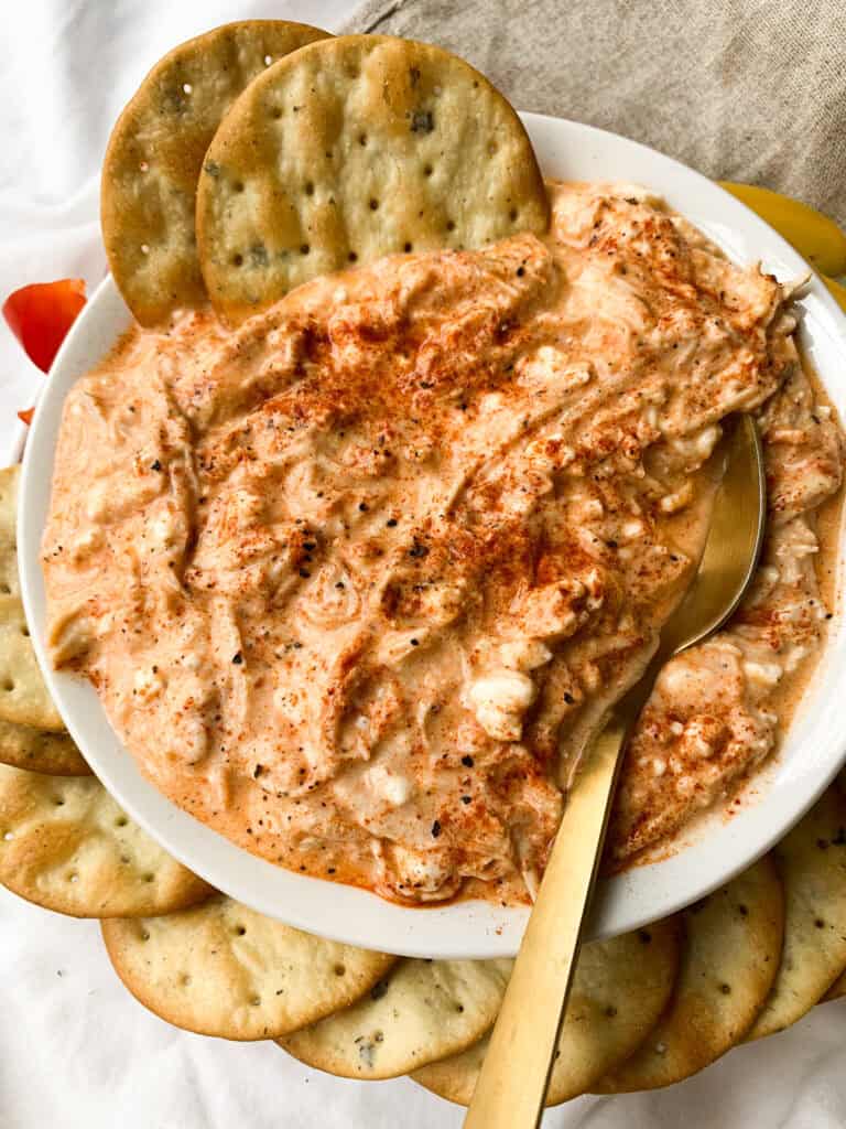 side view of a square bowl with healthy buffalo chicken dip in it with crackers and a spoon