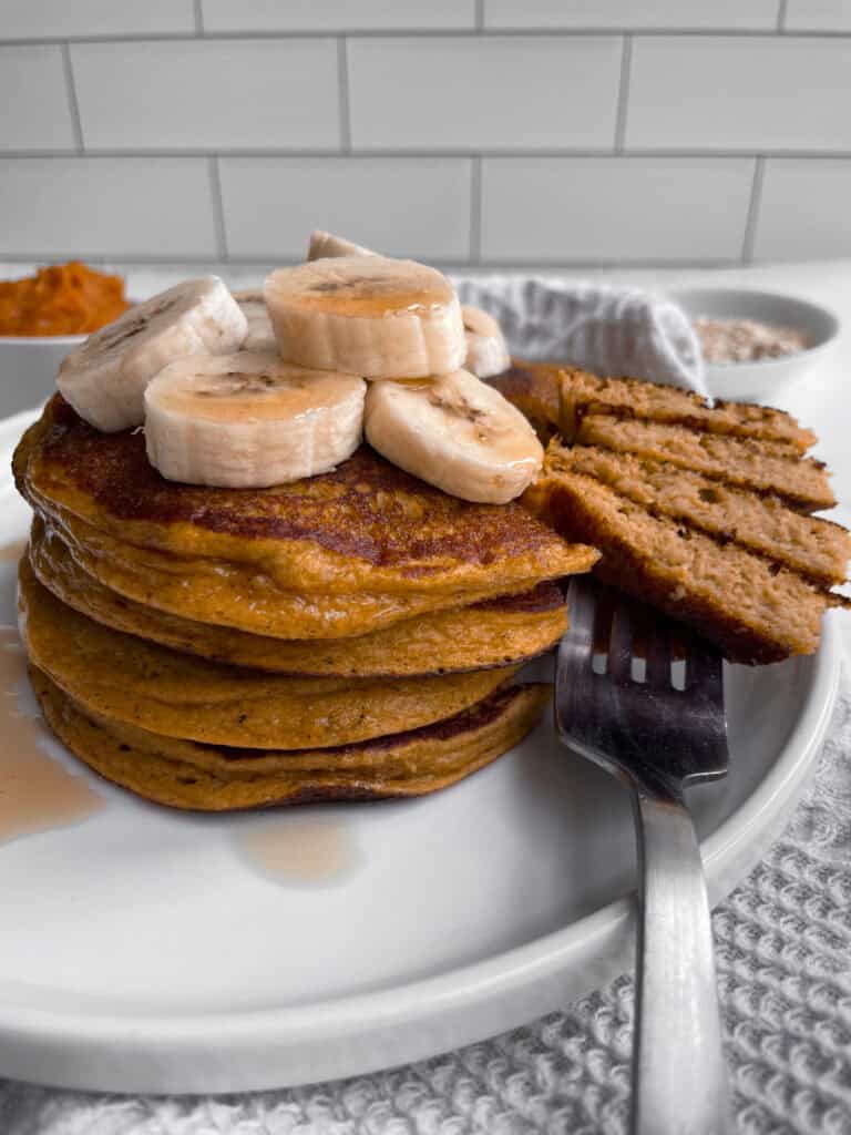 Cottage cheese pumpkin pancakes on a white plate with syrup and banana slices.