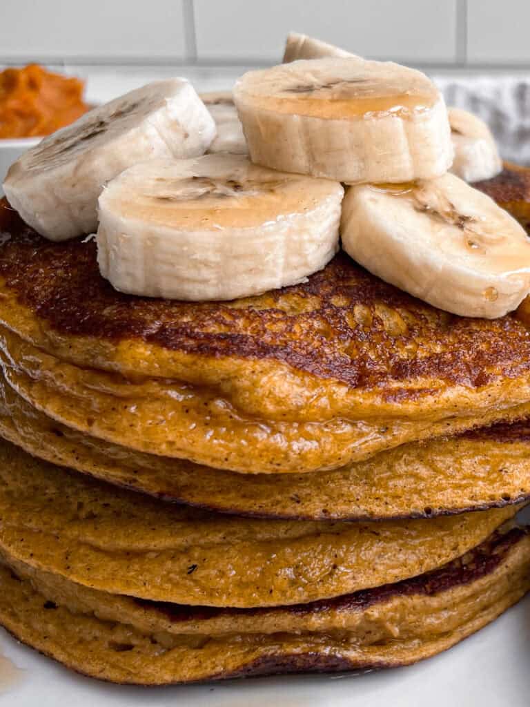 A stack of pumpkin cottage cheese pancakes topped with banana slices.
