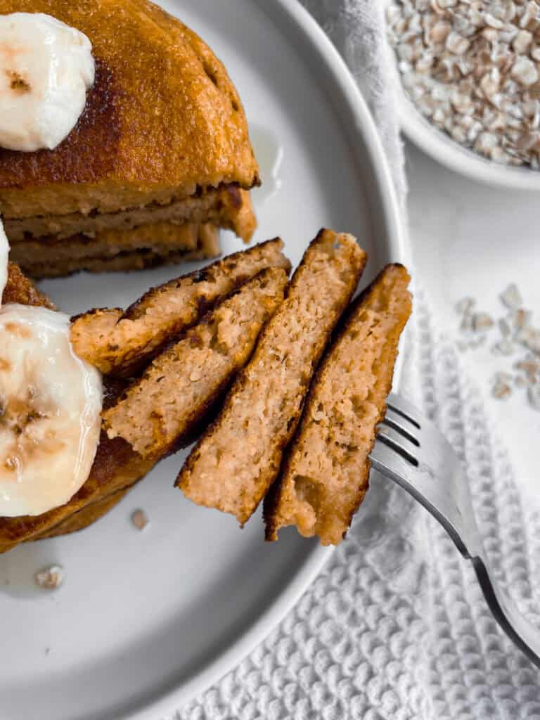 A bite of cottage cheese pumpkin pancakes on a fork next to the rest of the stack.