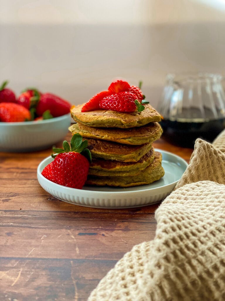 stack of vegan oat flour pancakes with maple syrup dripping on it and strawberries, wooden background