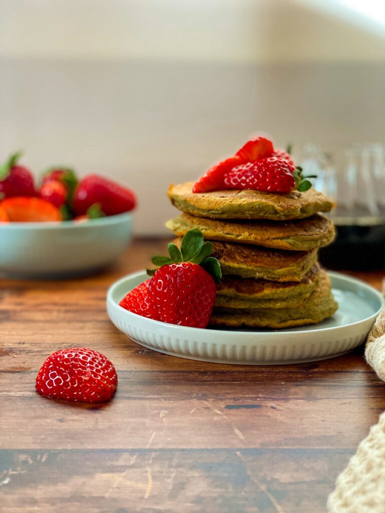 stack of vegan oat flour pancakes with maple syrup dripping on it and strawberries, wooden background