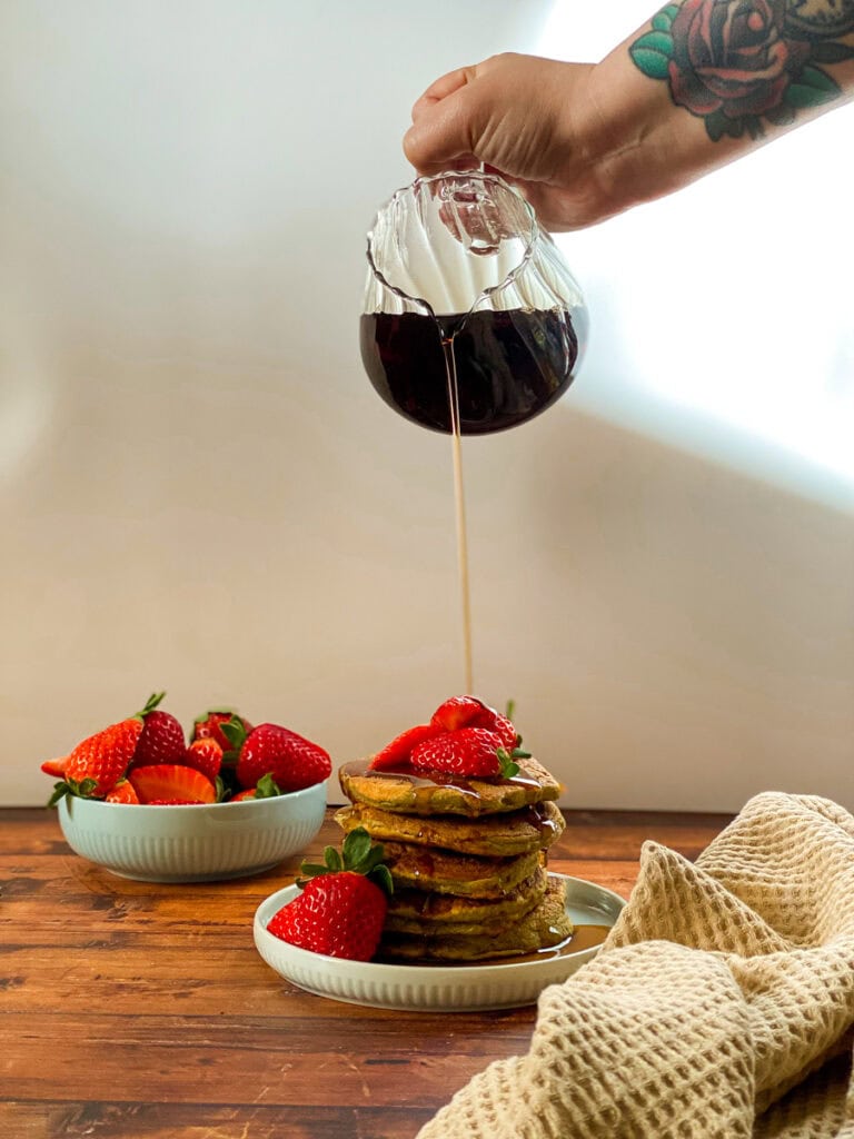 stack of pancakes with maple syrup dripping on it and strawberries, white background
