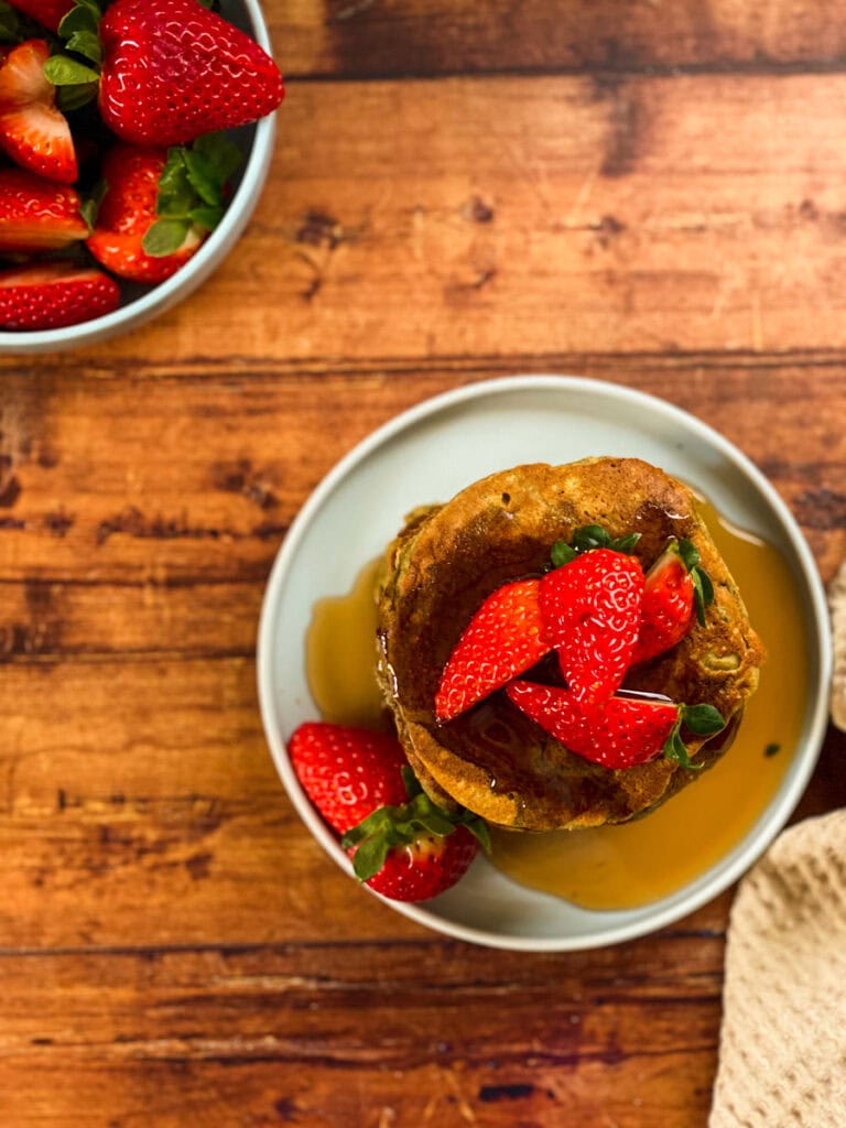 stack of vegan oat flour pancakes with maple syrup dripping on it and strawberries, wooden background