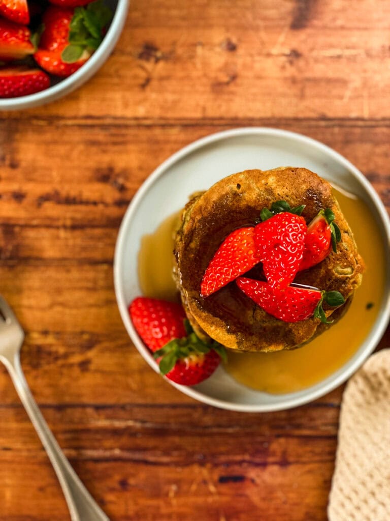 stack of vegan oat flour pancakes with maple syrup dripping on it and strawberries, wooden background