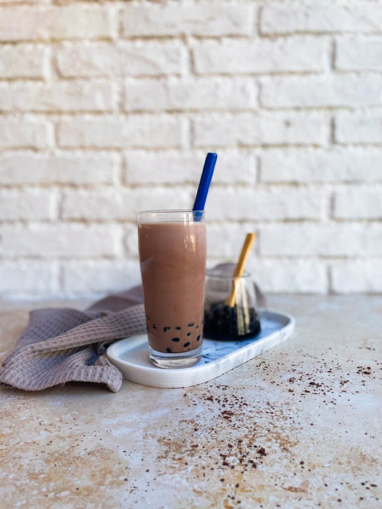 chocolate milk tea, boba pearls in a glass container behind, towel and marble tray under