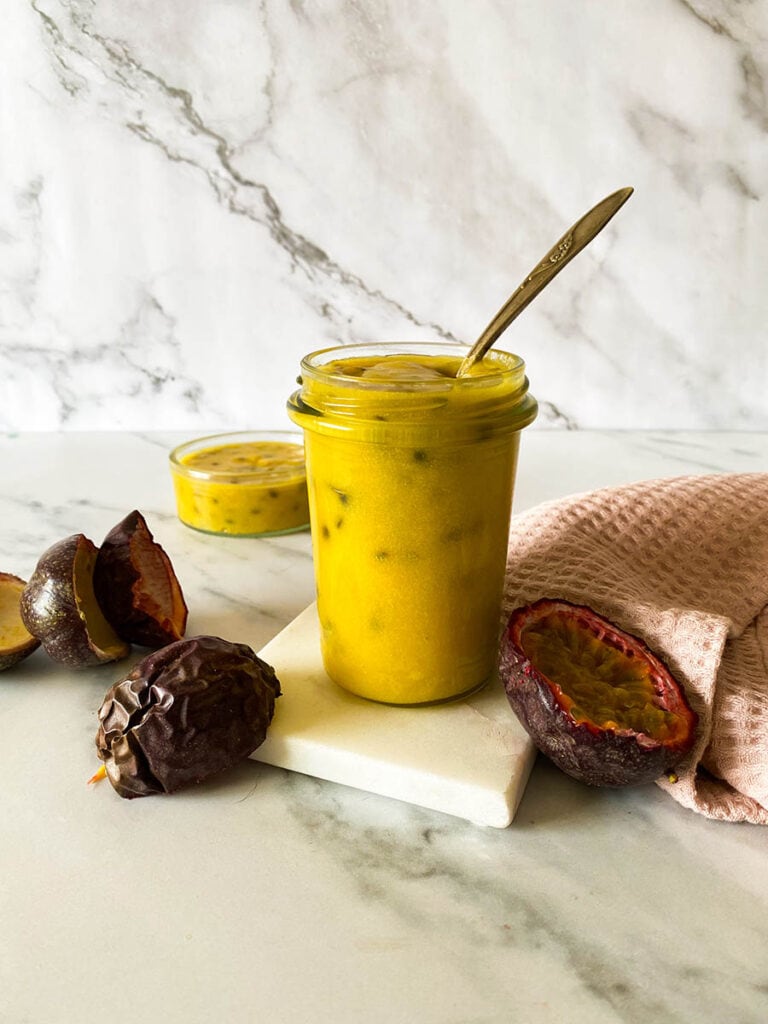 Passion Fruit Curd: Easy & Delicious 3 passion fruit curd jar on a marble background with a vintage spoon, with fresh passion fruits over a pink napkin