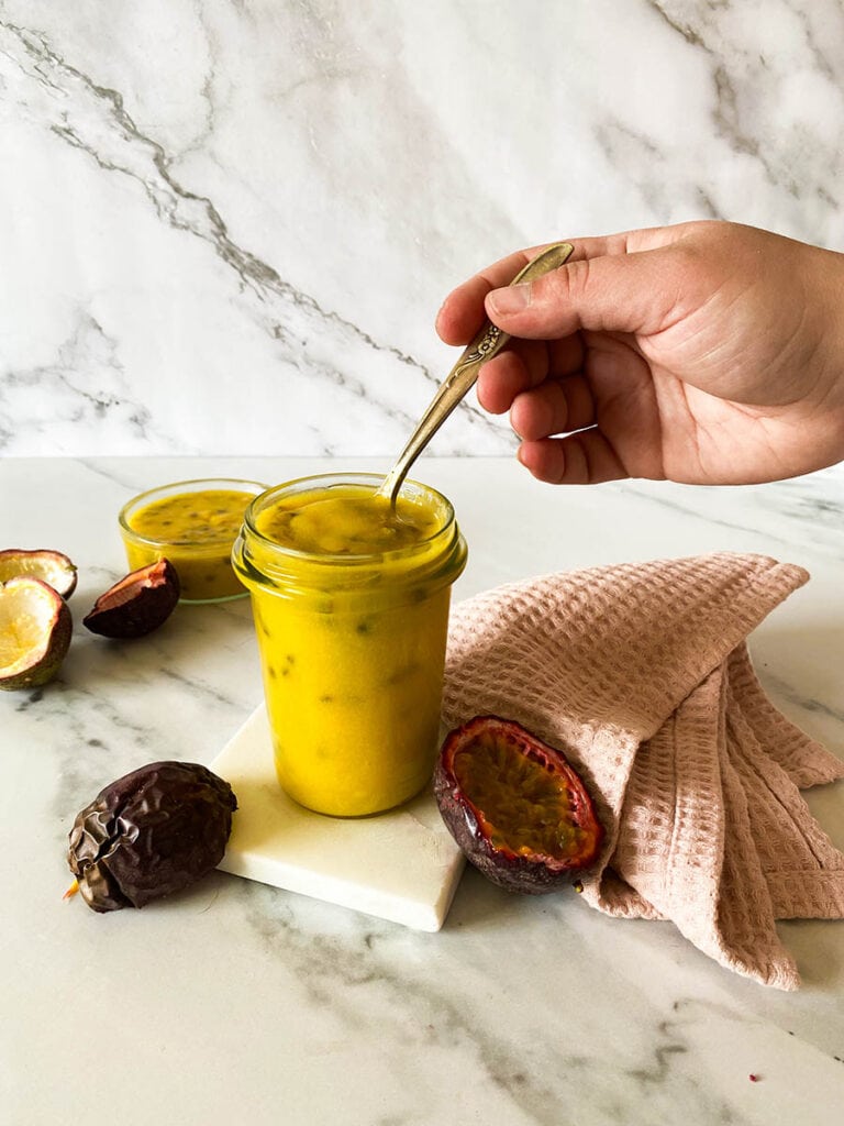 Passion Fruit Curd: Easy & Delicious 7 passion fruit curd jar on a marble background with a vintage spoon, with fresh passion fruits over a pink napkin