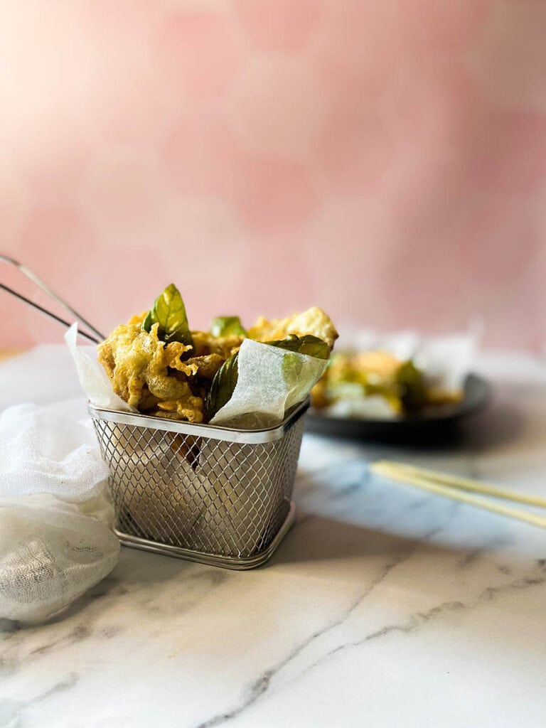 The #1 Best Popcorn Mushroom Recipe, Taiwanese-style 1 popcorn mushroom in a silver basket over some parchment paper, with extra dark dish and mushrooms on the background