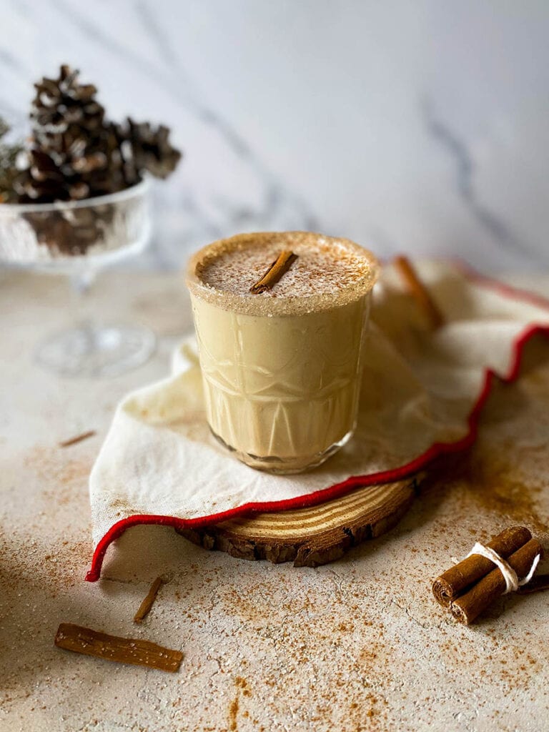 Baileys Eggnog: Get into the Holiday Spirit with a Creamy Cocktail 1 Baileys eggnog on a wooden slate with a white and red napkin, with pinecones and cinnamon sticks