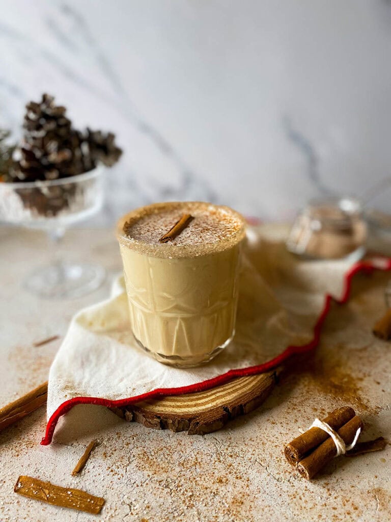 Baileys Eggnog: Get into the Holiday Spirit with a Creamy Cocktail 7 Baileys eggnog on a wooden slate with a white and red napkin, with pinecones and cinnamon sticks