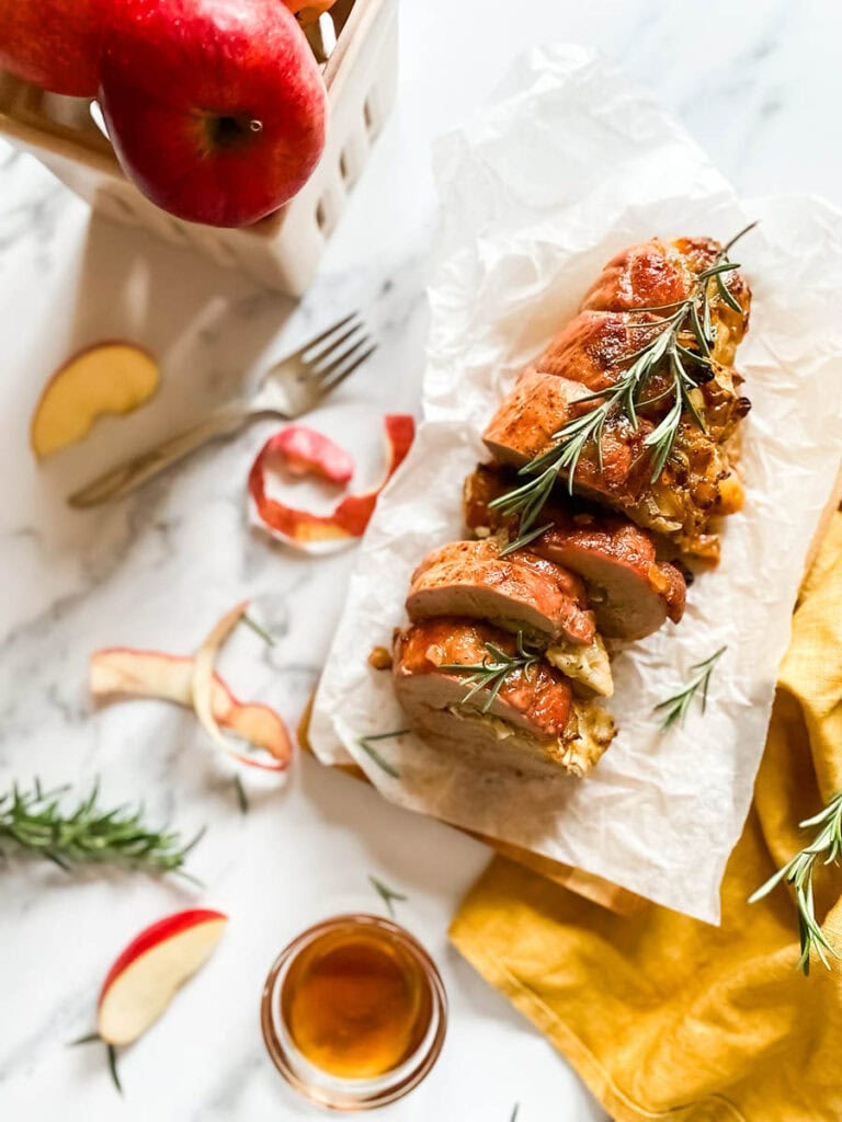 Brie Stuffed Pork Tenderloin Wonderland: A Delicious Holiday Delight 1 brie stuffed pork tenderloin fillet over parchment paper with apples and a fork over a wooden board