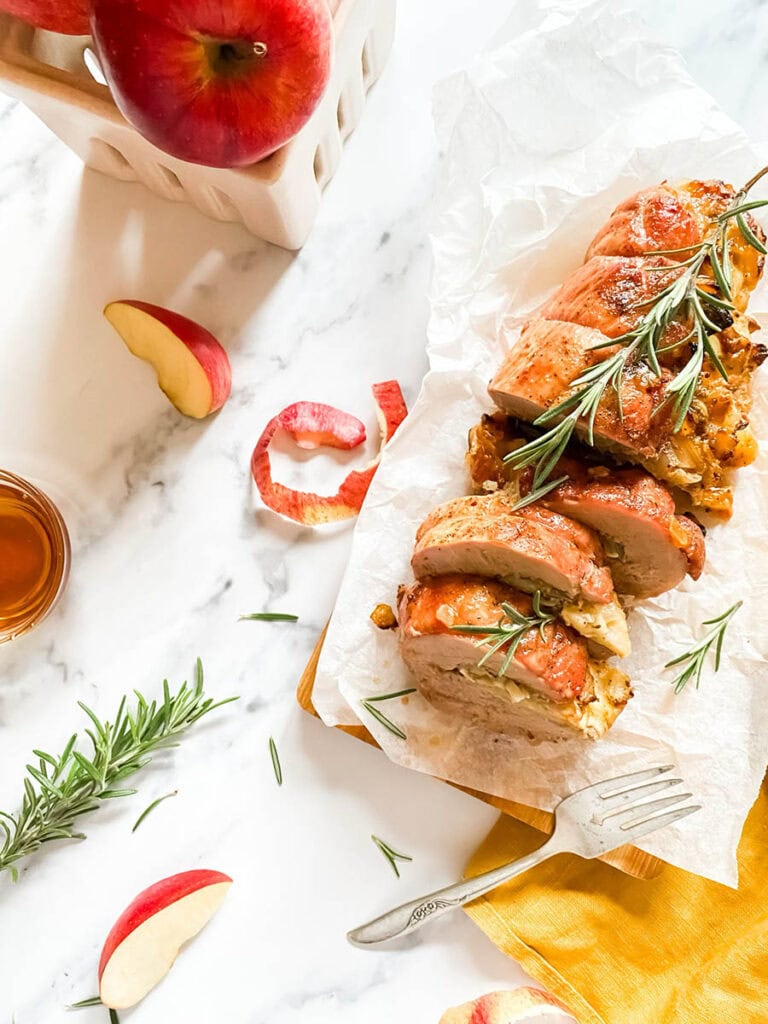 Brie Stuffed Pork Tenderloin Wonderland: A Delicious Holiday Delight 2 brie stuffed pork tenderloin fillet over parchment paper with apples and a fork over a wooden board