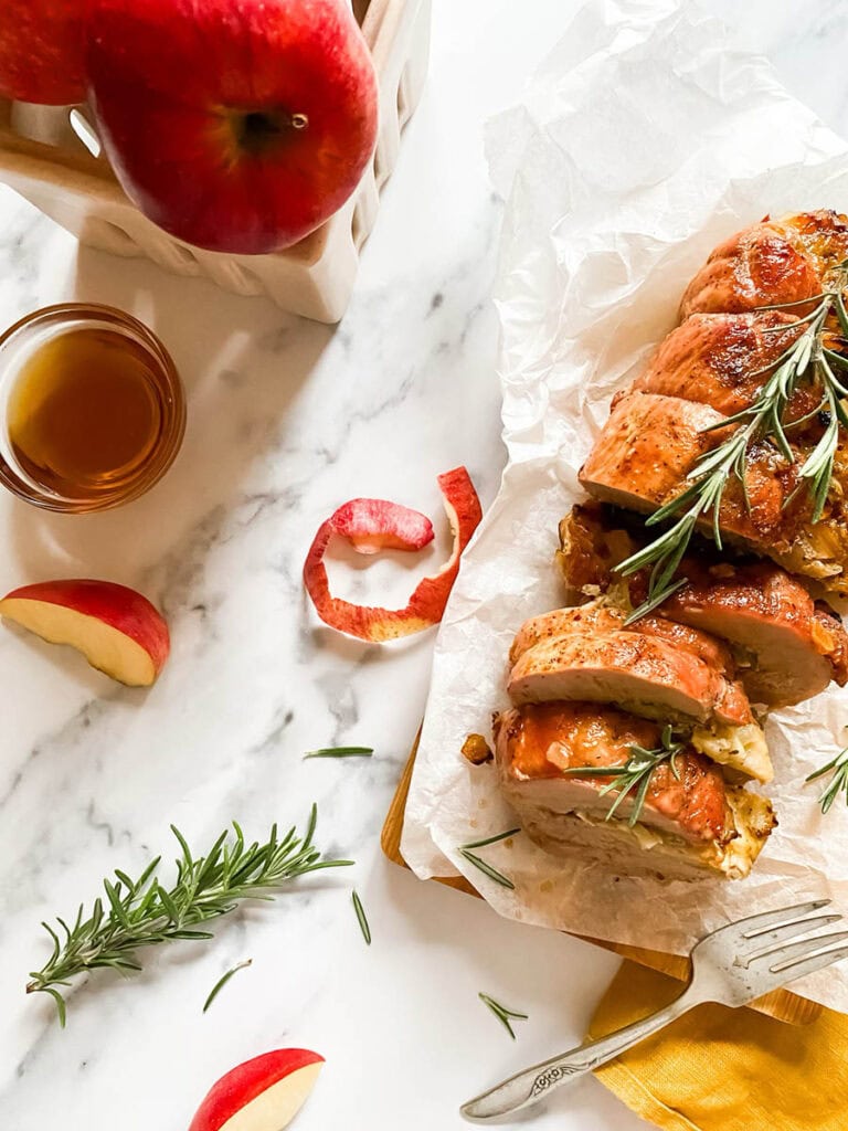 Brie Stuffed Pork Tenderloin Wonderland: A Delicious Holiday Delight 4 brie stuffed pork tenderloin fillet over parchment paper with apples and a fork over a wooden board
