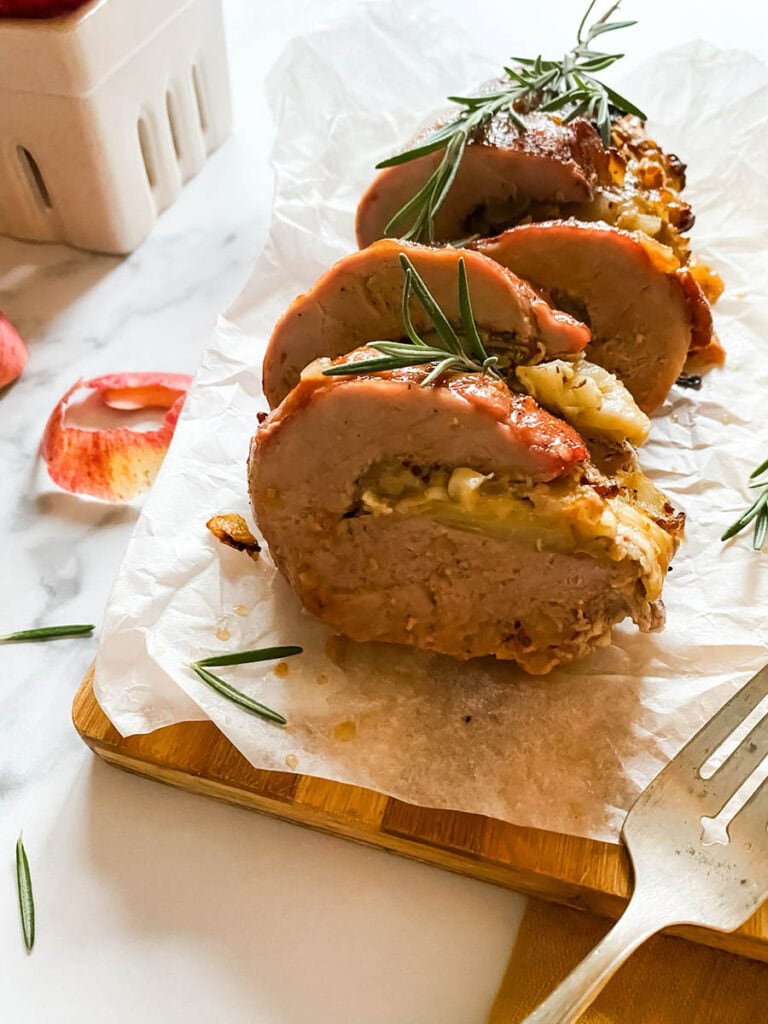 Brie Stuffed Pork Tenderloin Wonderland: A Delicious Holiday Delight 3 detail of brie stuffed pork tenderloin fillet over parchment paper with apples and a fork over a wooden board