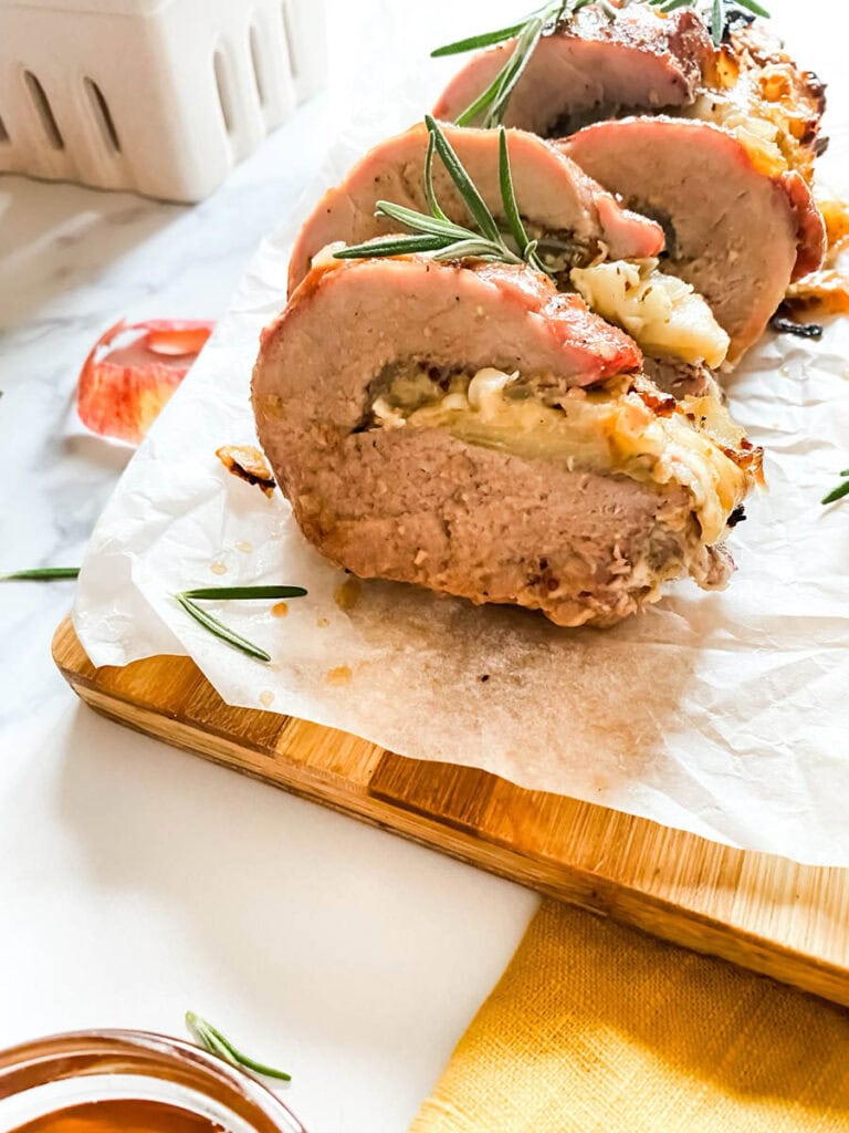 Brie Stuffed Pork Tenderloin Wonderland: A Delicious Holiday Delight 6 detail of brie stuffed pork tenderloin fillet over parchment paper with apples and a fork over a wooden board