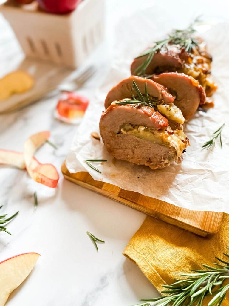 Brie Stuffed Pork Tenderloin Wonderland: A Delicious Holiday Delight 8 detail of brie stuffed pork tenderloin fillet over parchment paper with apples and a fork over a wooden board