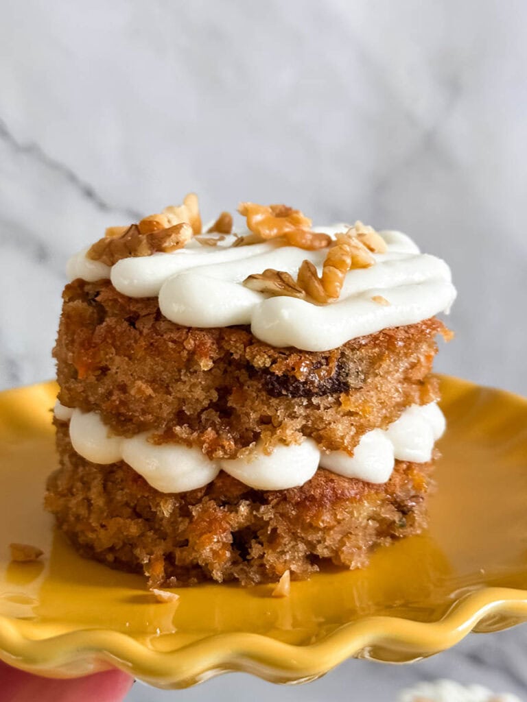 Mini Carrot Cake Recipe, The Perfect Easter Dessert 3 Side view of a two-layer mini carrot cake with visible shredded carrots and pecans, stacked with piped cream cheese frosting and garnished with walnuts.