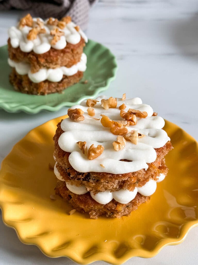 Mini Carrot Cake Recipe, The Perfect Easter Dessert 9 A beautifully plated mini carrot cake, sitting on a bright yellow plate with piped frosting and crunchy walnuts, while other cakes are arranged in the background.