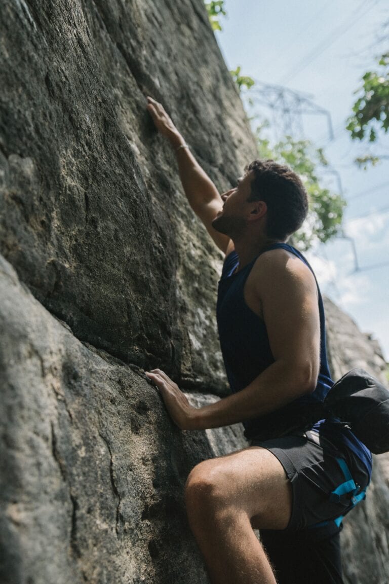 Focused man in athletic gear rock climbing outdoors, showcasing determination and strength.