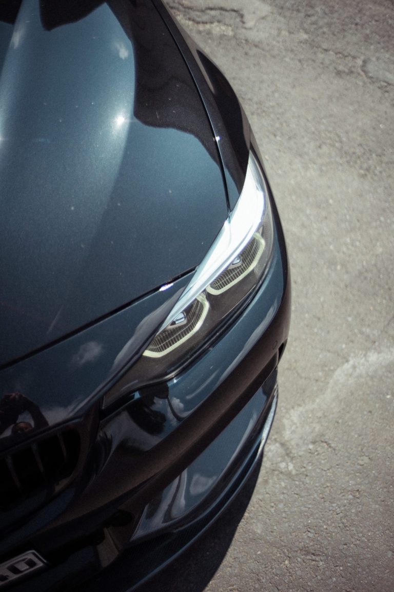 Nahaufnahme der Frontpartie eines schwarzen Autos mit markantem LED Scheinwerfer und glänzender Motorhaube auf einem grauen Asphaltuntergrund.