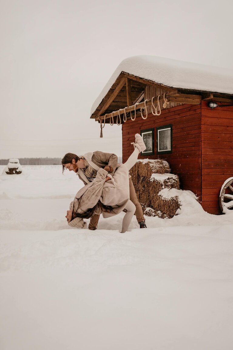 A couple joyfully dances outside in a snowy winter landscape, creating a warm, romantic scene.