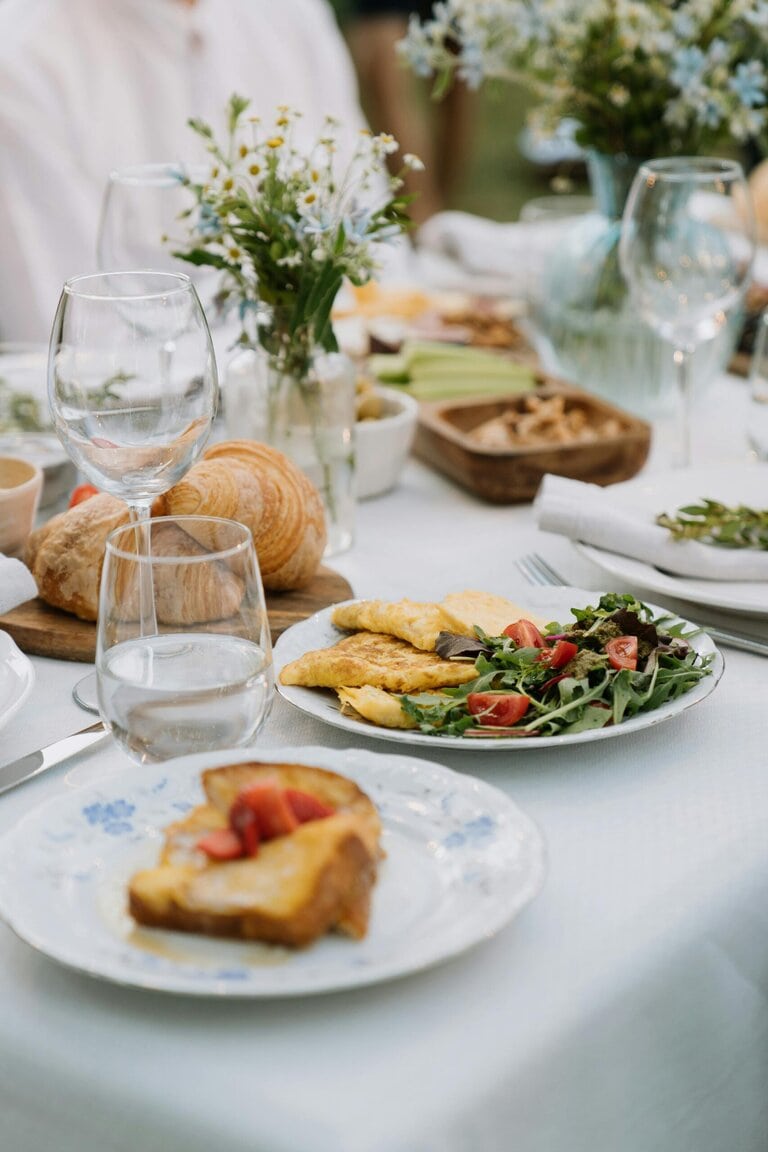 A summer table set outdoors with wine, fruit, and a rustic meal, evoking a French long lunch.