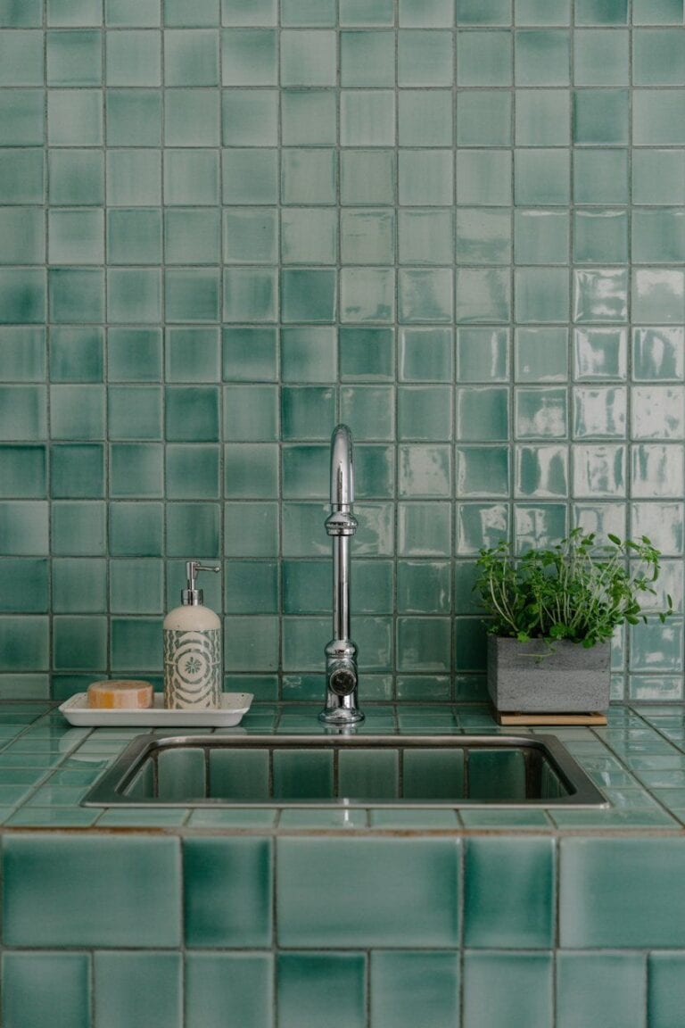 Green tiled corner sink with faucet, soap dispenser, and plant; corner sink kitchen decor ideas