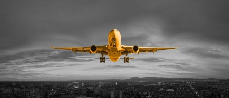 A black and white image with an orange airplane flying through the sky