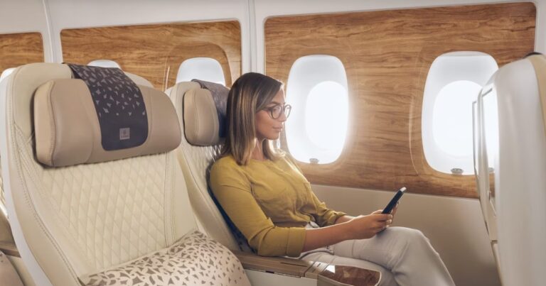 Passenger looking at phone while enjoying Emirates premium economy seating and cabin