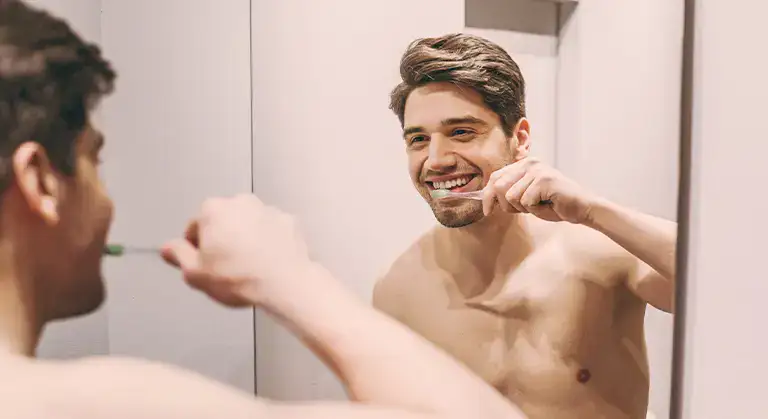 Uśmiechnięty mężczyzna myjący zęby w łazience - zdjęcie.