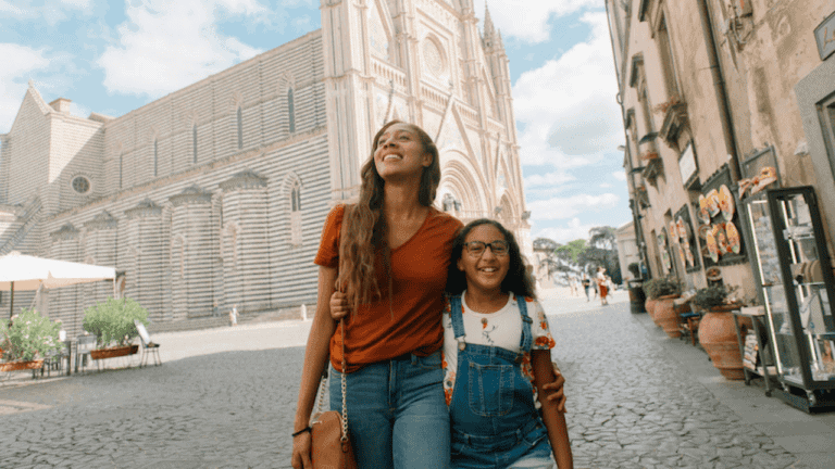 Smiling woman and girl enjoying sightseeing in a historic city street, embracing travel trends.