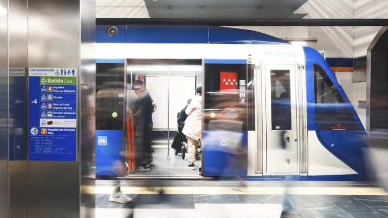 Un tren del Metro de Madrid en una estación, con personas entrando y saliendo, y señalización visible en la pared.