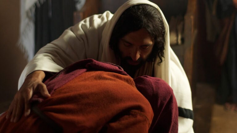 Two people embracing in a dimly lit room, one in white and the other in reddish-brown.