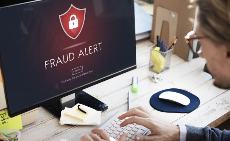 Man in a suit sitting in front of a desktop screen that says "FRAUD ALERT"