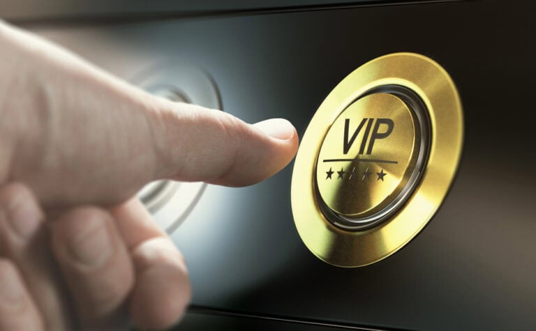 A person's thumb pressing a gold elevator button with the letters "VIP" on it