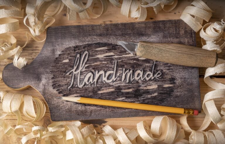 Holzpaddle mit der Gravur „Handmade“, Schnitzwerkzeug und Holzspänen – Symbol für einen sexpositiven Workshop zum Holzpaddle-Schnitzen in Stuttgart.
