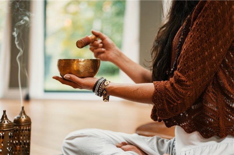 Singer using singing bowl for meditation and spiritual awakening, cozy indoor setting with incense.