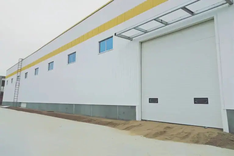 White industrial sectional door installed on a warehouse exterior, engineered to meet ANSI/DASMA 102 standards for thermal insulation and structural performance.