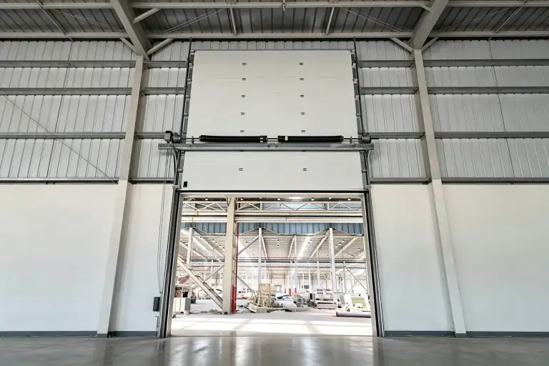 Interior view of a high-performance industrial sectional door featuring European-standard hardware, torsion springs, and universal tracks installed in a modern manufacturing facility.