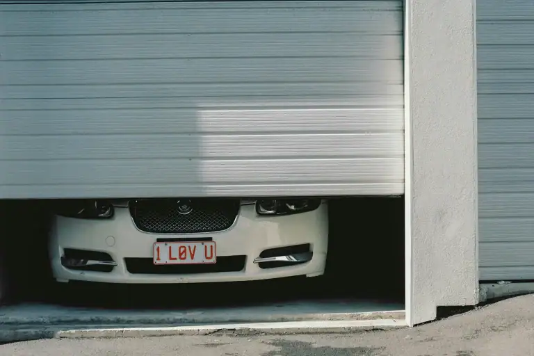 A vehicle positioned under a commercial sectional door, illustrating the high risk of bottom panel impacts. ABX offers OEM commercial sectional door bottom section replacements and auto-recovery upgrades to restore structural integrity.
