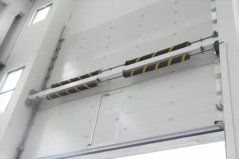 Detailed interior installation view of a heavy-duty sectional door for the AVIC project, highlighting the robust torsion spring system with safety warning tape and an integrated wicket door engineered for strict aerospace facility standards.