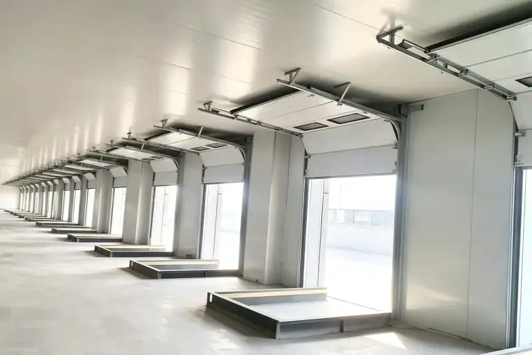 Modern commercial logistics facility featuring a row of white sectional overhead doors and hydraulic dock levelers for efficient warehouse operations.