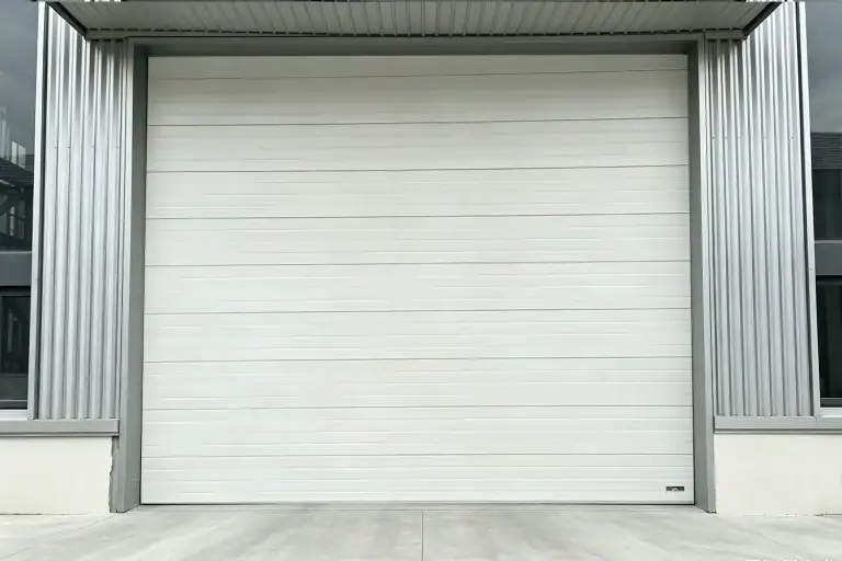 White commercial sectional overhead door installed on a modern industrial warehouse with corrugated metal siding and an overhead canopy.
