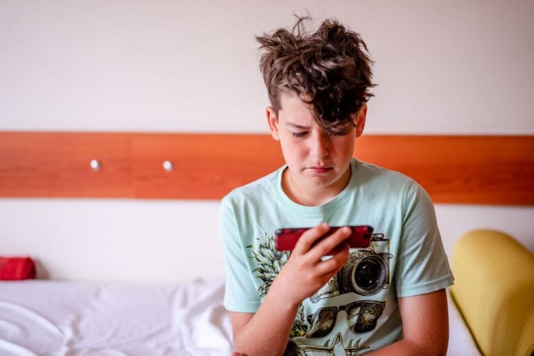 A teenage boy in a casual t-shirt focused on his smartphone indoors.